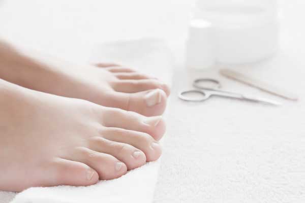 Zwei Füße auf einem weißen Handtuch und im Hintergrund liegen Nagelpflegeprodukte