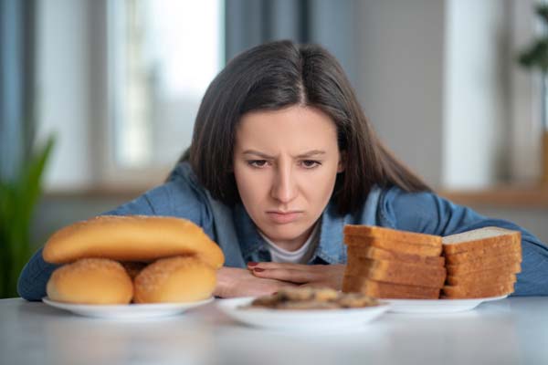 Eine Frau sitzt vor glutenhaltigen Lebensmitteln und kann sie wegen ihrer Zöliakie nicht essen.