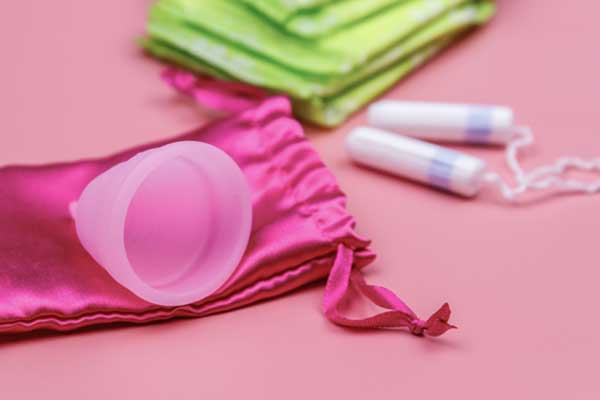 Menstruationstasse liegt auf einem Beutel. Im Hintergrund liegen Tampons.