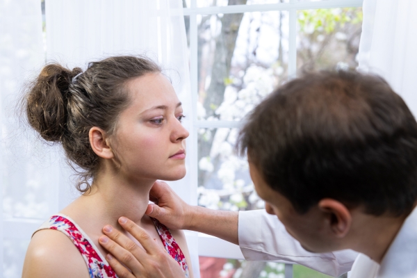 Ein Arzt untersucht die Schilddrüse einer Patientin.