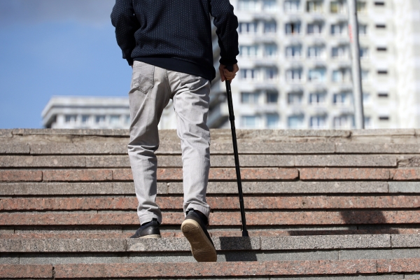 Ein älterer Mann mit einem Gehstock geht eine Treppe hinauf.